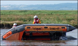 The weight of the crewmembers pulling the ropes rights the capsized lifeboat