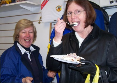 Customer Linda Green enjoying a piece of cake celebrating the launch of the shop watched by RNLI Supporters' group chairman Jendy Weekes