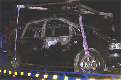 The fire-damaged car being lifted onto a tow truck at the scene of the incident