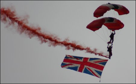 With smoke trailing behind, Red Devils members Steve Candlish and Jeff Bull unfurl the Union Jack during their approach to Burnham's VE/VJ anniversary event