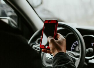 person holding red smartphone sitting in front of vehicle steering wheel